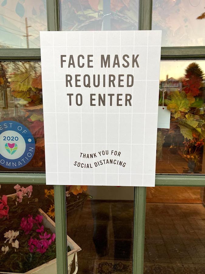A sign on the front door of the store that reads "face mask required to enter. Thank you for social distancing."