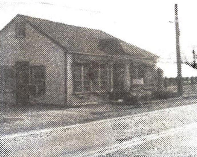 A grainy black and white image of a small building sitting on a roadside.