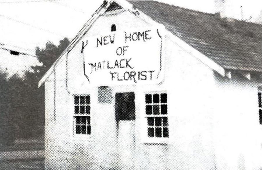 A grainy image of a white building on the side of a road. There is a sign hanging above the door that says "New home of Matlack Florist."
