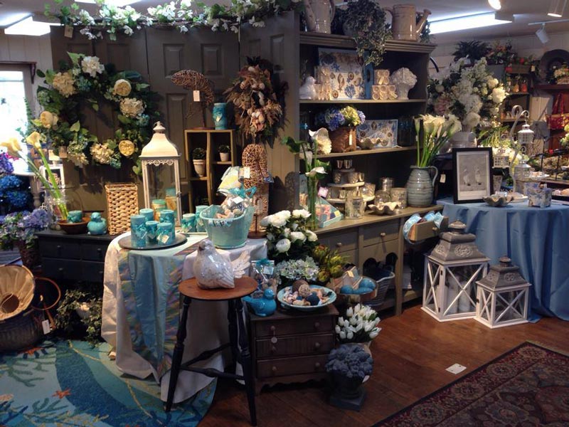 An image of the Matlack gift shop. A variety of home decor, wreaths, and trinkets are arranged on tables and shelves. Most of the items are blue, white, and green.