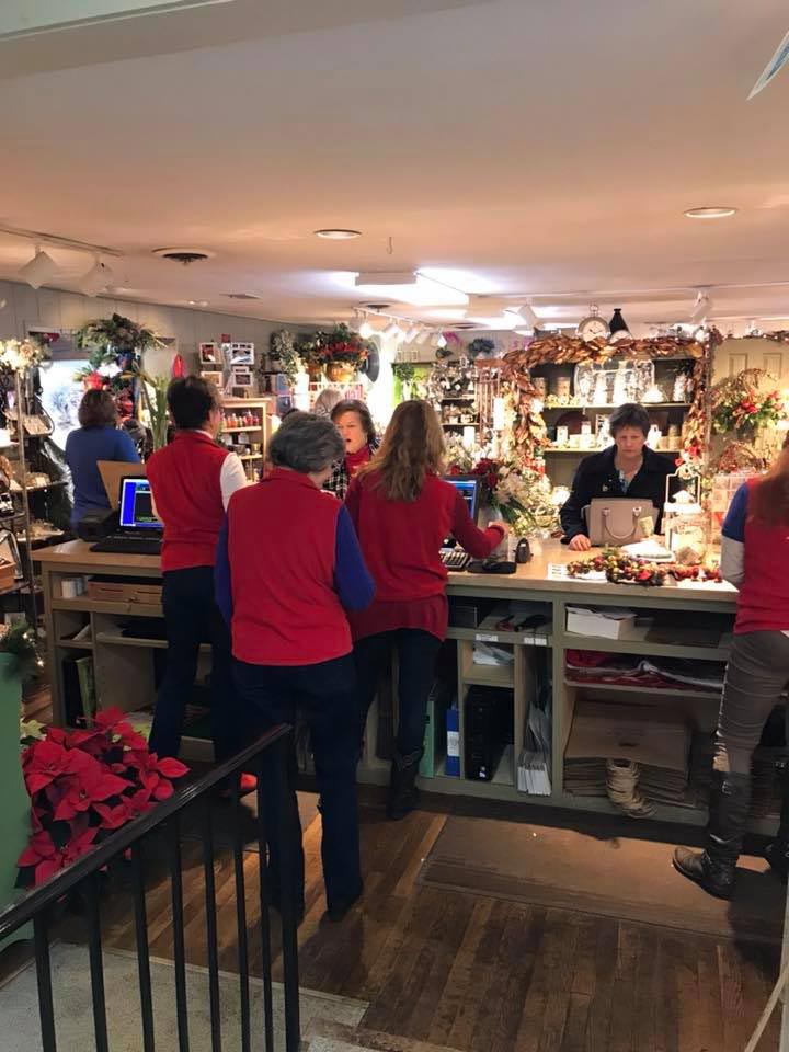 An image taken from behind the registers in the gift shop. Four salespeople in red vests assist customers.