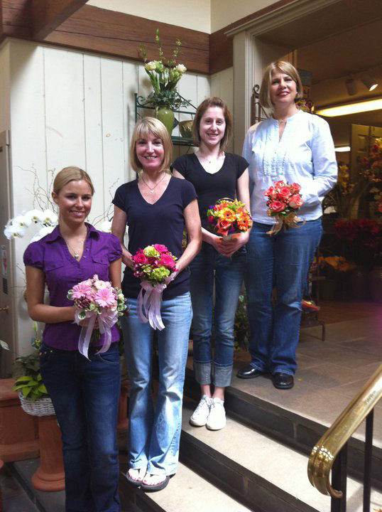 Four salespeople stand on a row of steps holding prom bouquets.