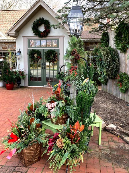 A photo of the storefront during the holidays. There are wreaths on the double doors and red and green plants in front.