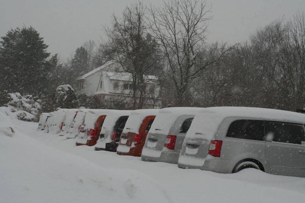 10 vans sit in a snow covered parking lot.